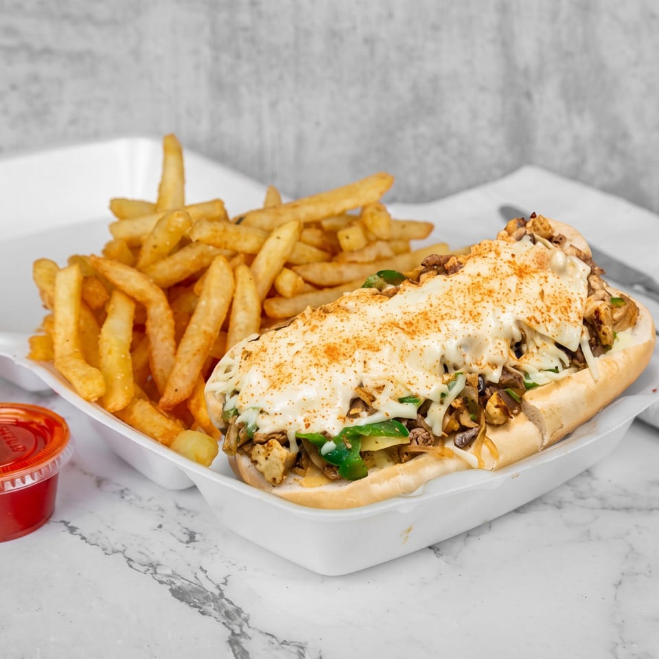 Cheesesteak sandwich with fries and two dipping sauces in a white takeout container.