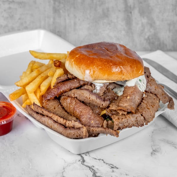 A large gyro sandwich with fries and two dipping sauces in a white takeout container.